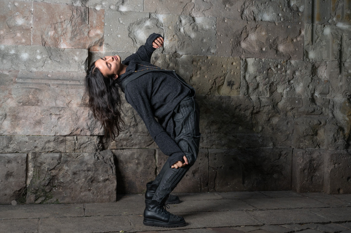 Model in a black outfit arching her body against a stone wall