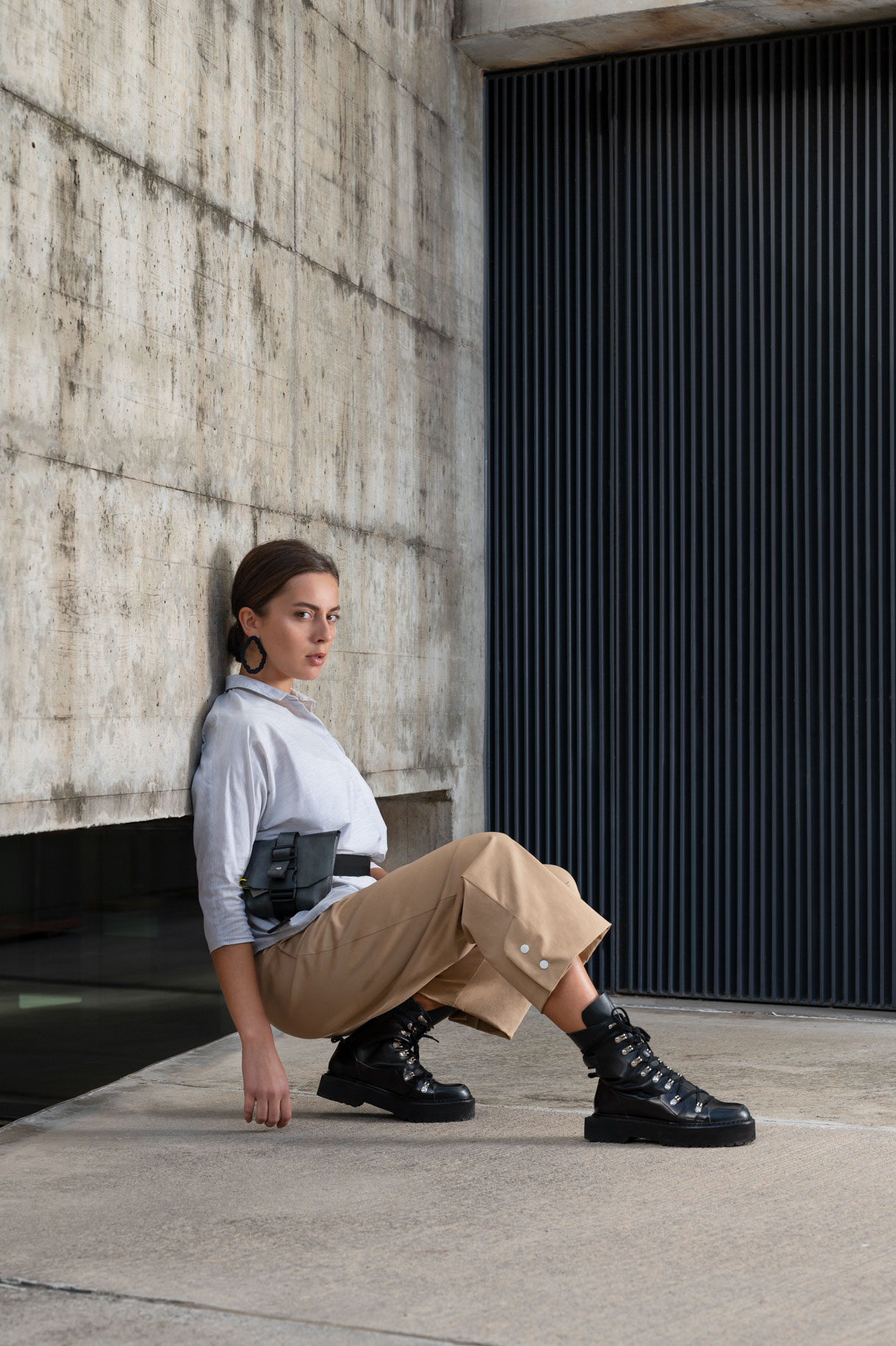 Model seated on the floor in camel trousers and a grey shirt