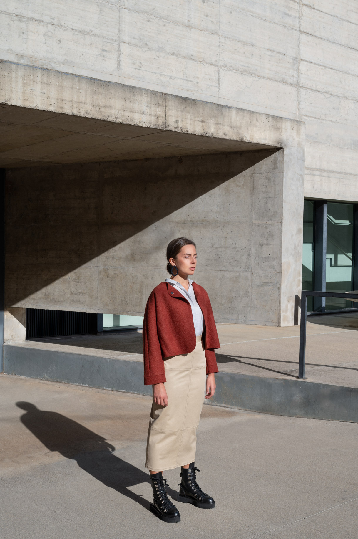 Model in a burgundy jacket and beige skirt in front of a concrete building