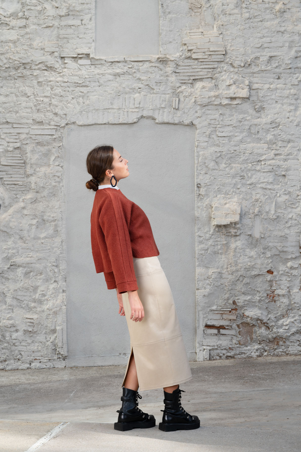 Model in profile in a burgundy jacket and knitted skirt against a white wall