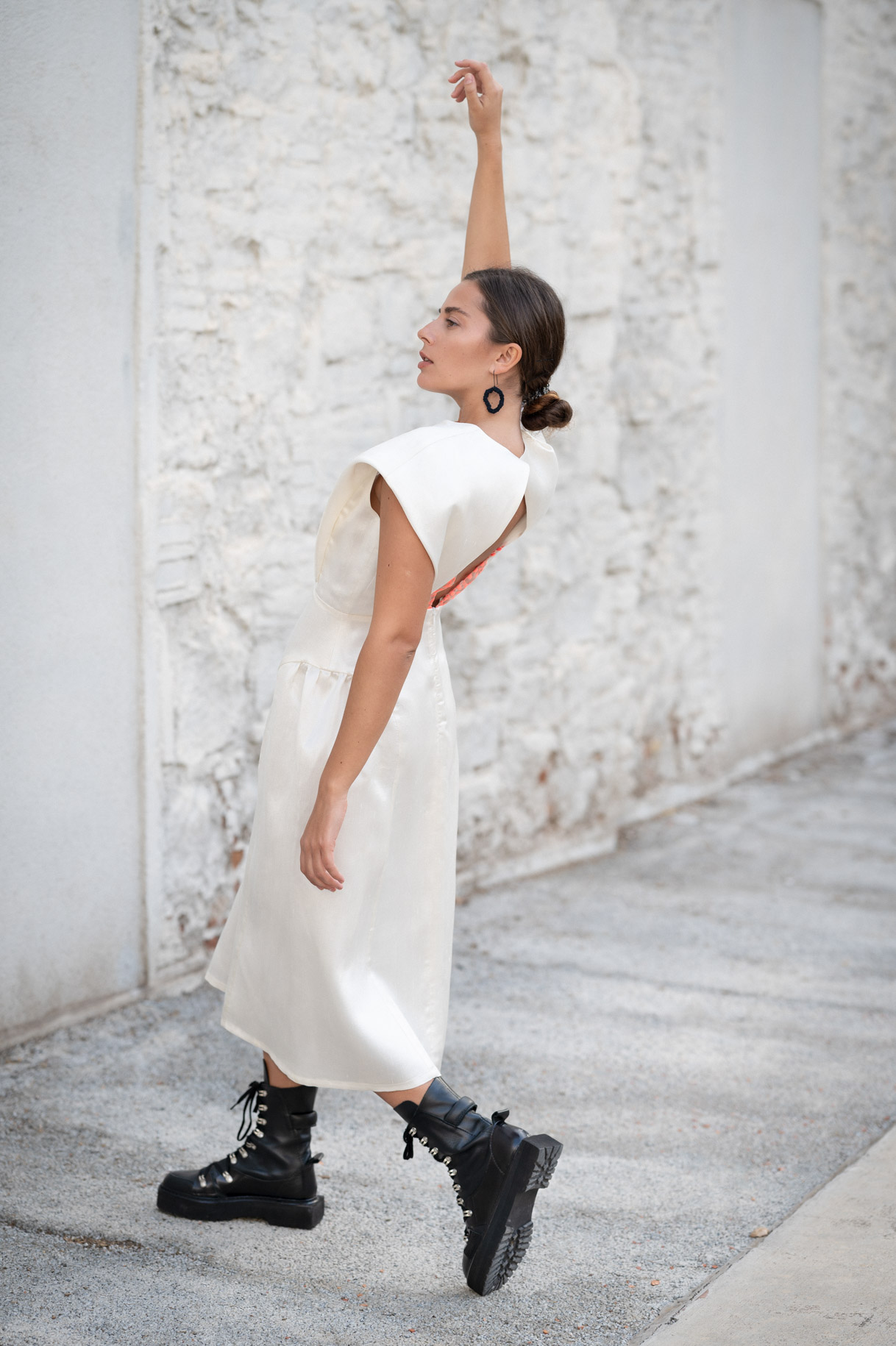 Model in a white dress and black boots raising her arm