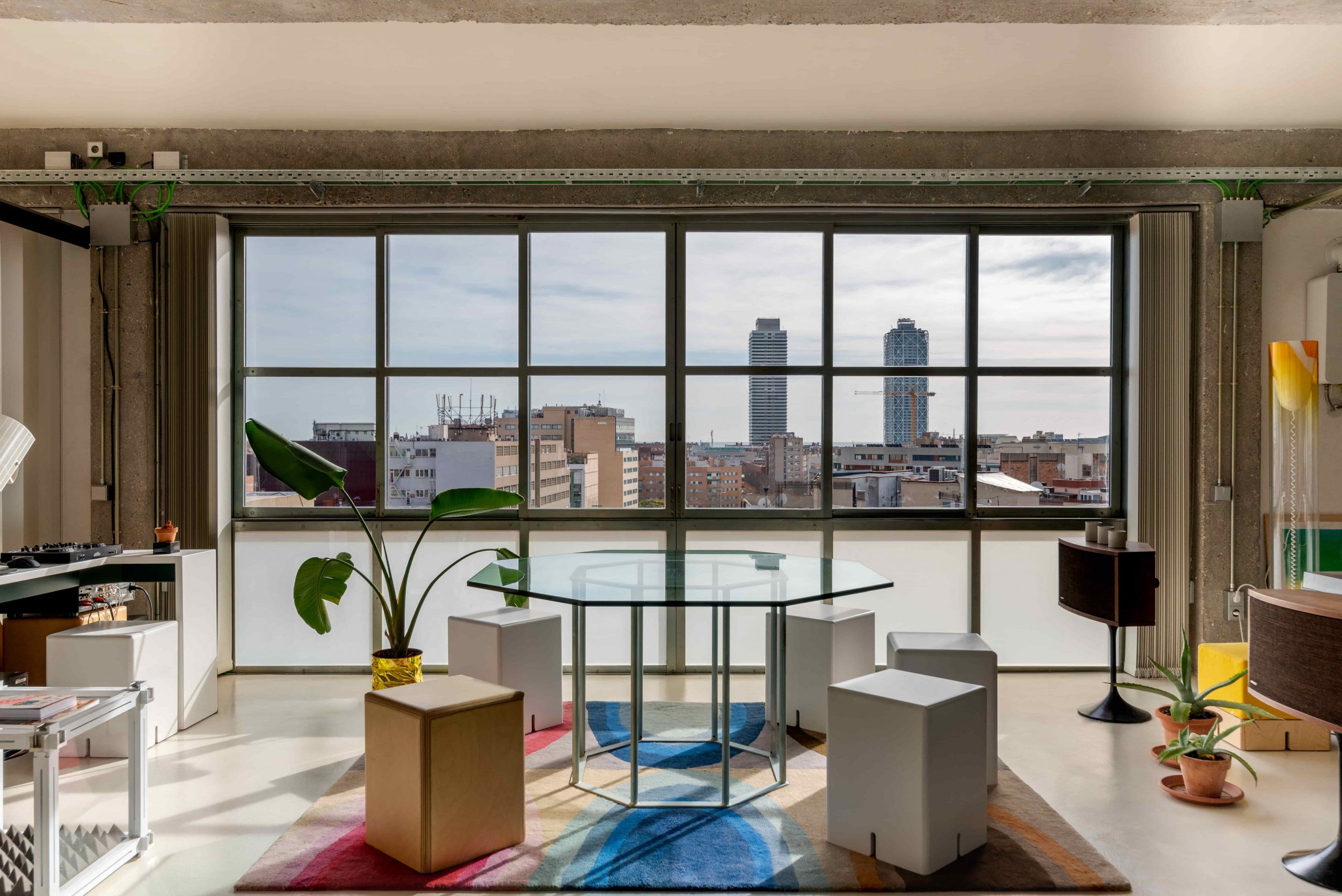 Salón de un loft industrial con ventanales de suelo a techo sobre los tejados de Barcelona