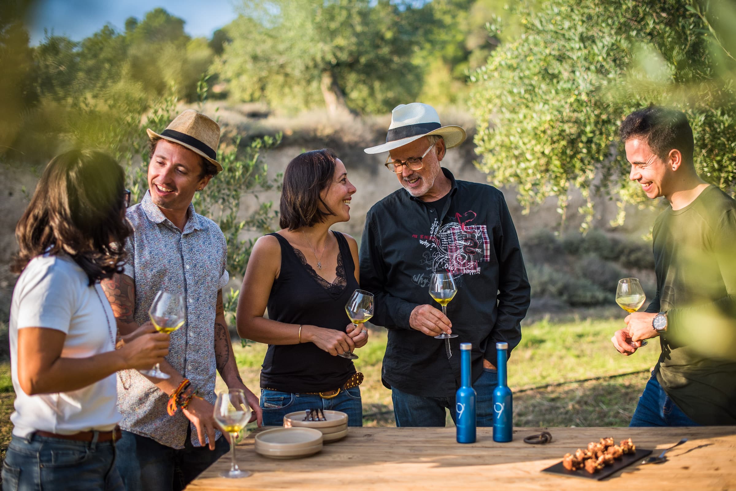 Grupo de asistentes conversando con copas de cata en un olivar