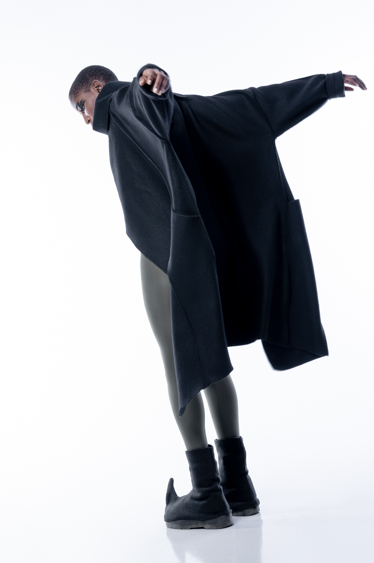 Model in an oversized black coat and leggings in motion