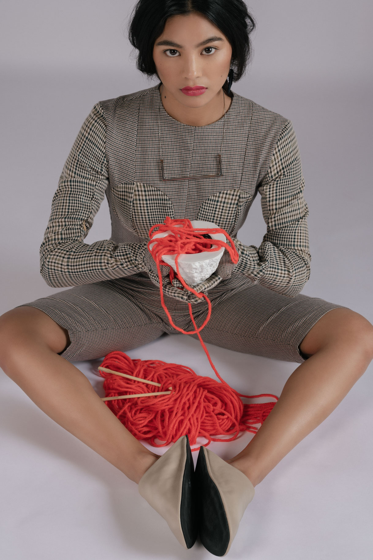 Model seated in a checked dress holding a skein of red wool