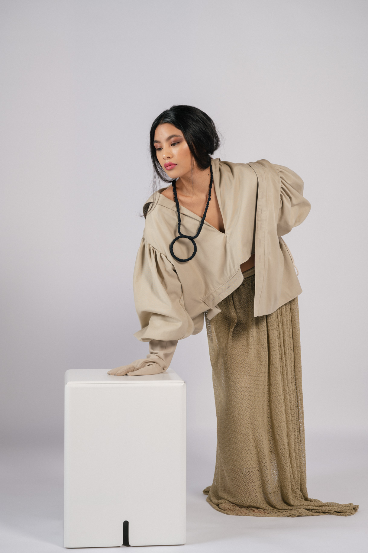 Model in a beige outfit and necklace leaning on a white cube